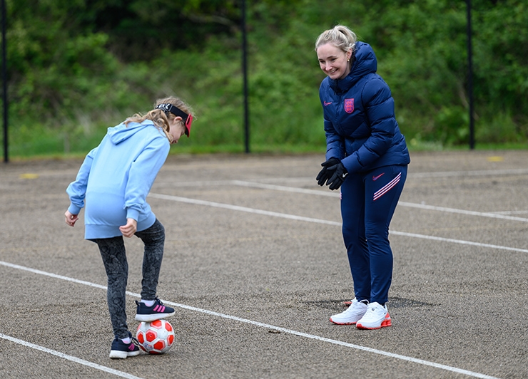 A woman encourages a young girl while playing football in a playground