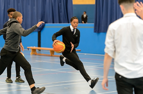 Teenage boys play basketball in school uniform in a sports hall