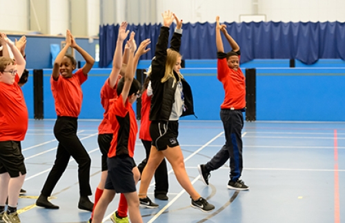 A teacher leads a group of pupils in a stretching exercise