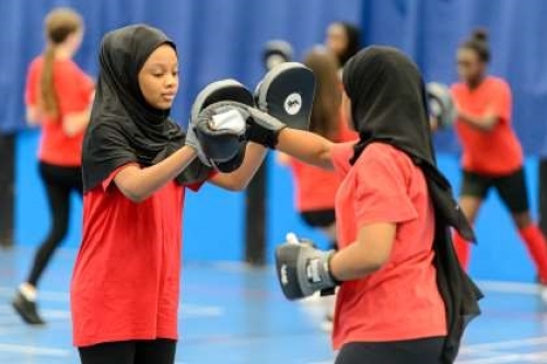 Two girls. wearing dark headscarves and bright red tops, practice their boxing moves in an exercise session