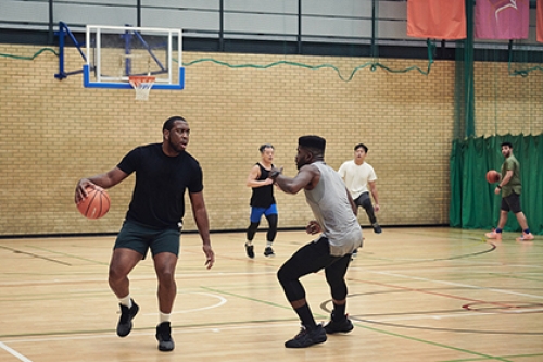 Two men play basketball in a sports hall