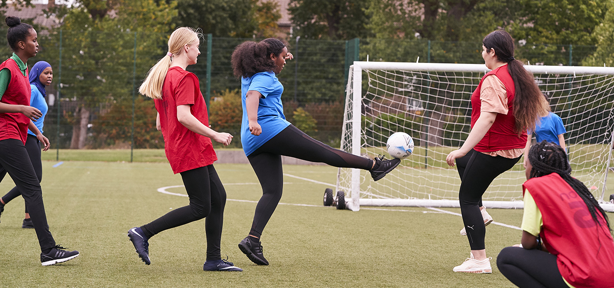 A group of girls play football on an artificial pitch.