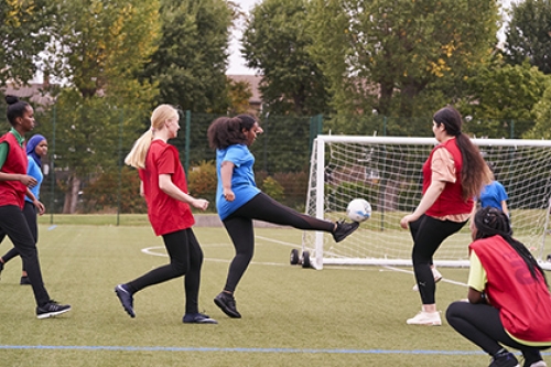 A group of girls play football on an artificial pitch.