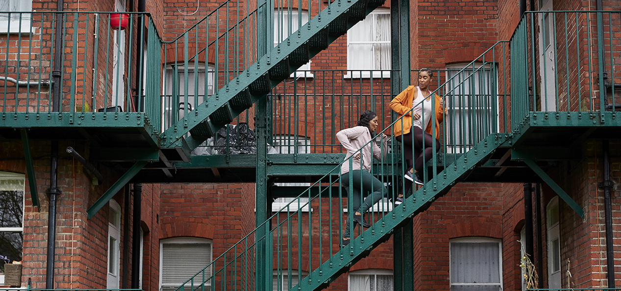 Two women running up stairs within a housing complex.