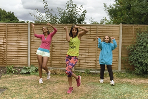 Three women perform Zumba exercises in a garden.