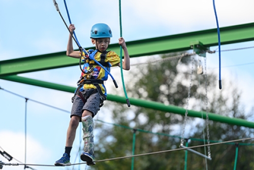 A boy with a prosthetic leg balances on a high ropes course.