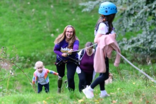 A woman smiles while pulling a rope to climb a hill. A girl in a helmet is at the top of the hill and there are other climbers below.