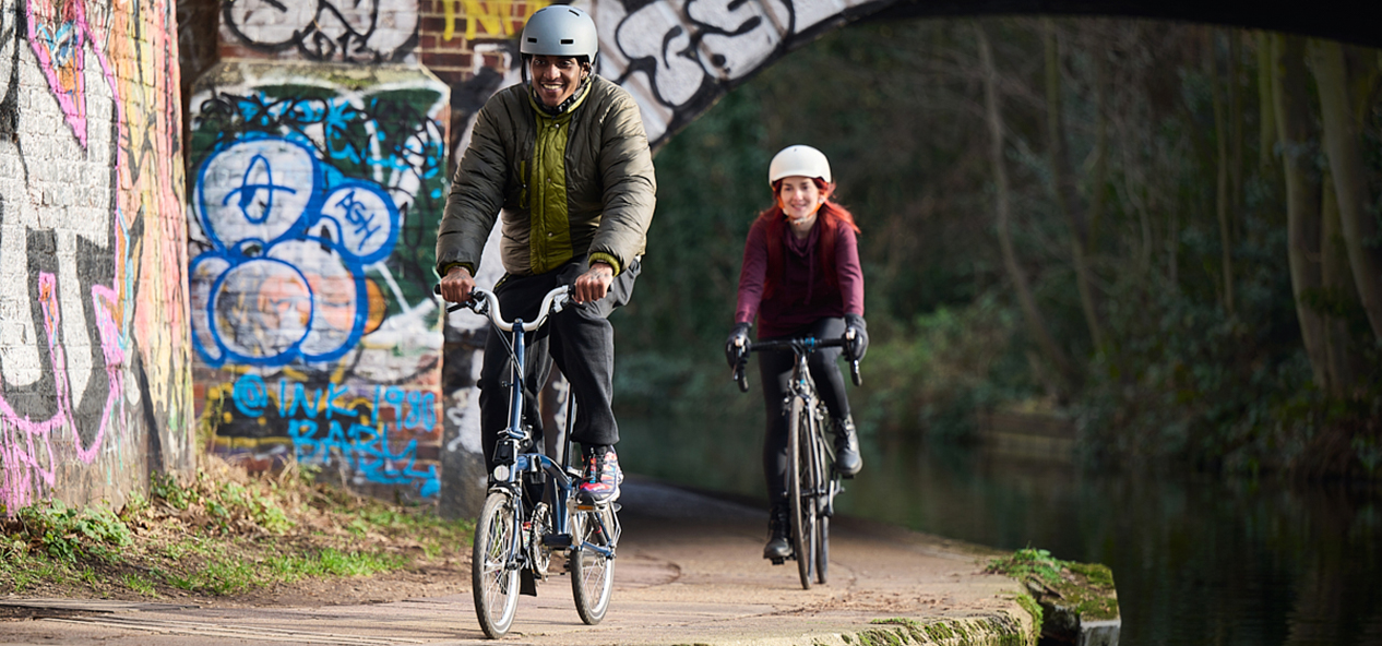 A man and a woman cycle on a canal towpath