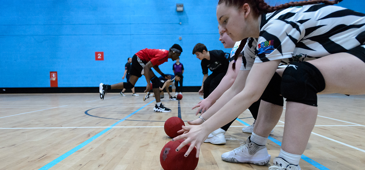 A group of young people reach down to pick up dodgeballs at the start of a game