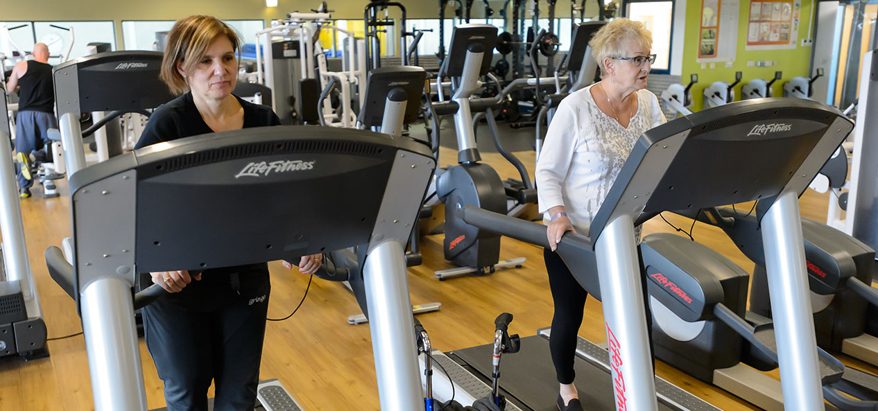 Two women walk on treadmills in a gym