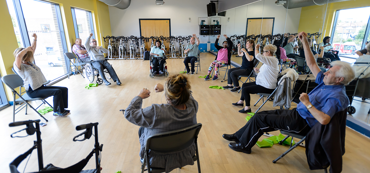 A group of older people perform seated exercises while in a circle in an exercise studio