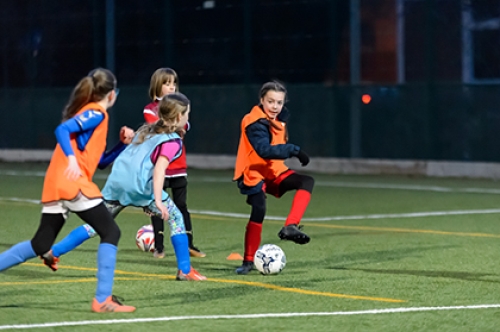 A group of girls play football on an artificial pitch.