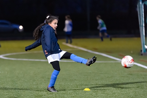 A girl kicks a football on an outdoors pitch.