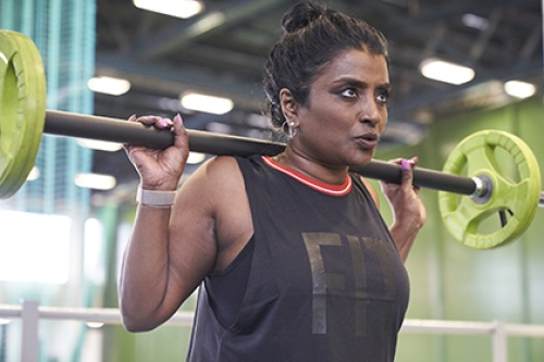 A woman squats using a barbell in a gym