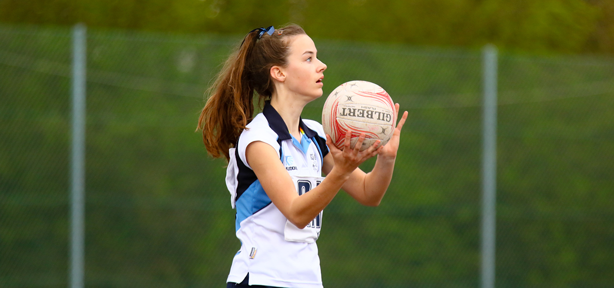 A girls plays netball outside.