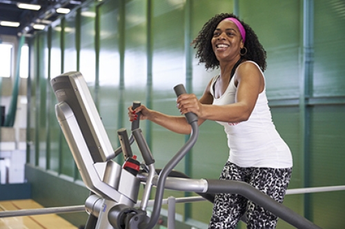 A smiling woman exercises on an elliptical trainer in a gym.