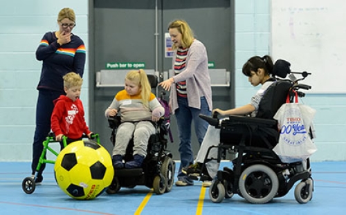 Two child wheelchair users and a and a boy with a walking frame play with a giant football