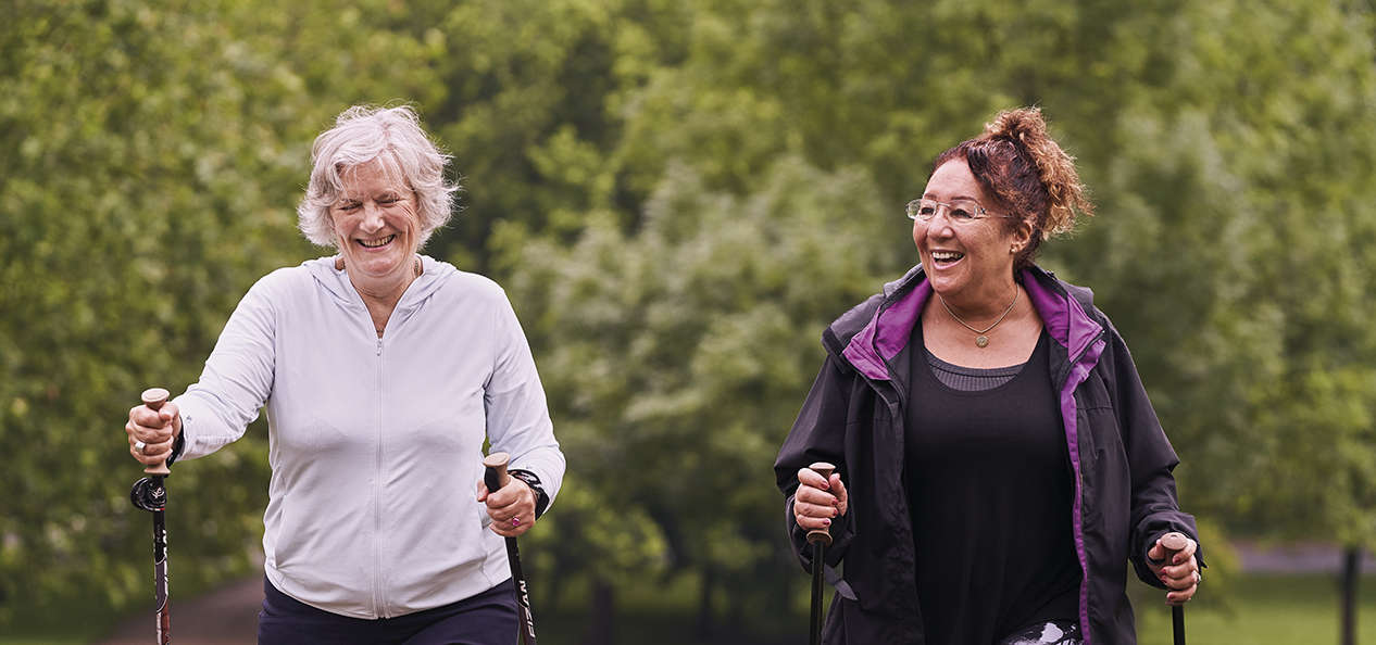 Two women, with walking poles, walk in a park