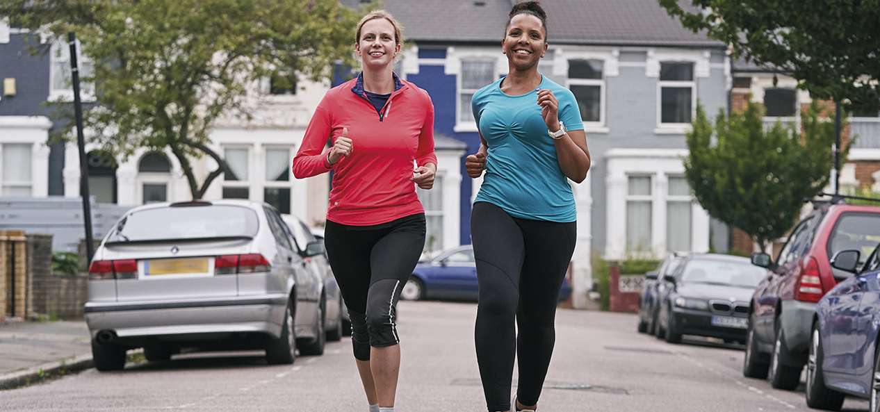 Two women run side-by-side down a road.