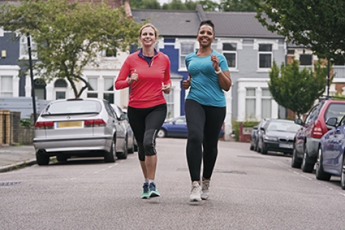 Two women run side-by-side down a road.