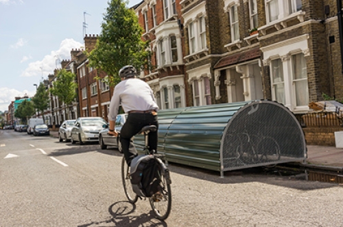 Cyclist (motion blurred) passing lockable on-street bike storage