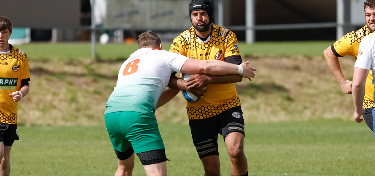 Two men play mixed ability rugby on an outdoors pitch on a sunny day.