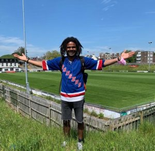 A man stands with his arms raised at the corner of a non-league football stadium pitch