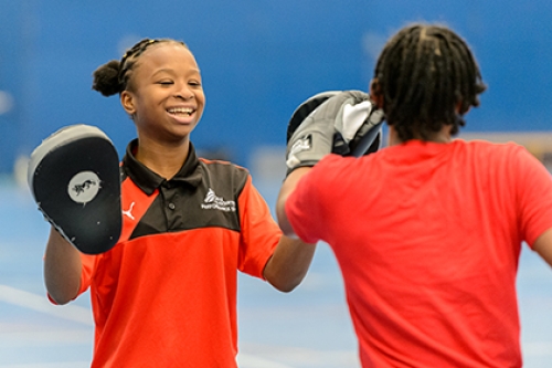 Two schoolgirls boxing inside a sports hall.