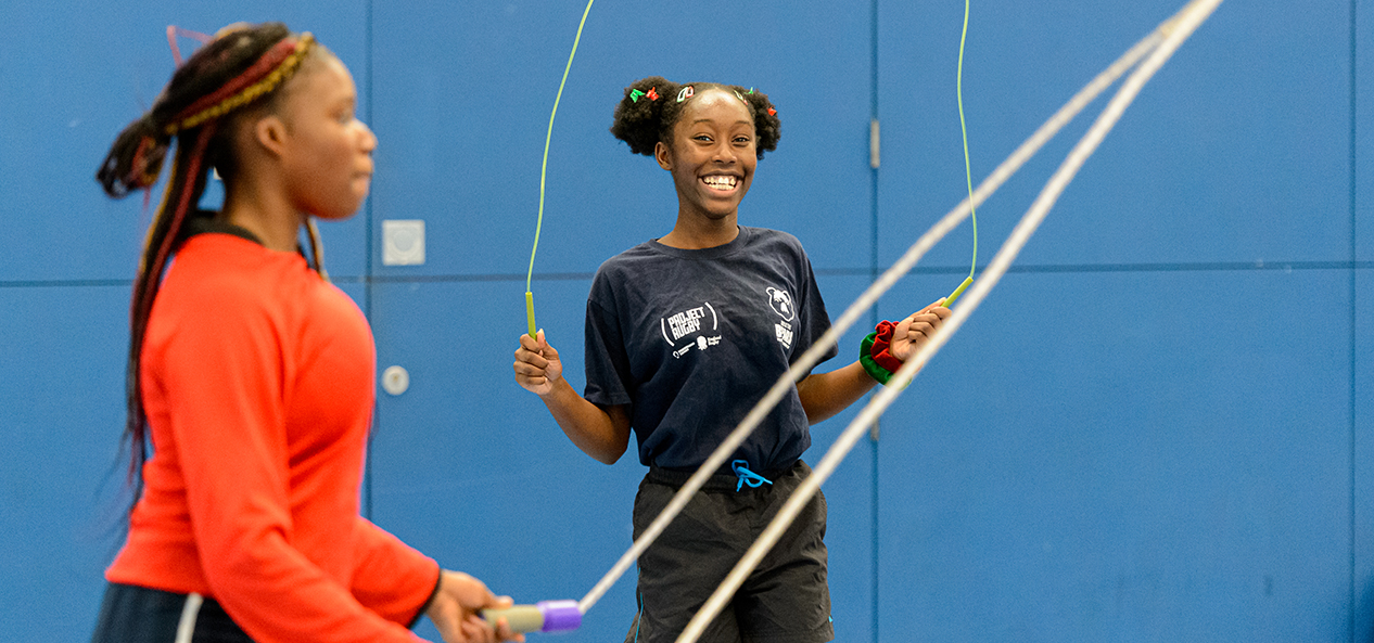 Two children skipping inside a school sports hall.
