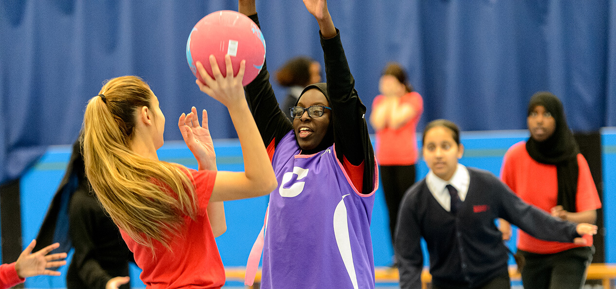 A group of schoolchildren playing netball inside a sports hall.