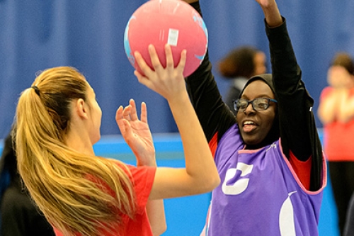Two schoolchildren playing netball inside a sports hall.