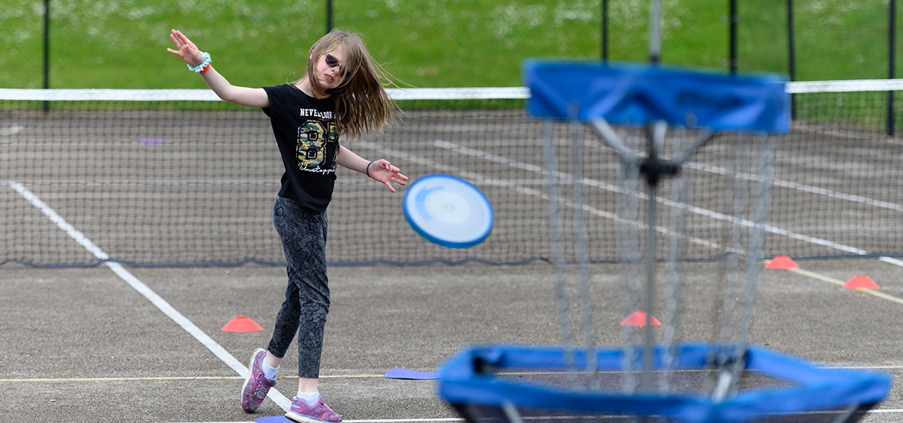 A visually impaired girl throws a frisbee at a target in a playground.