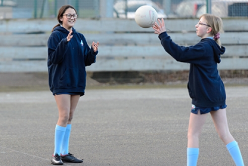 A schoolgirl throws a ball towards another girl during an outdoor game of netball.