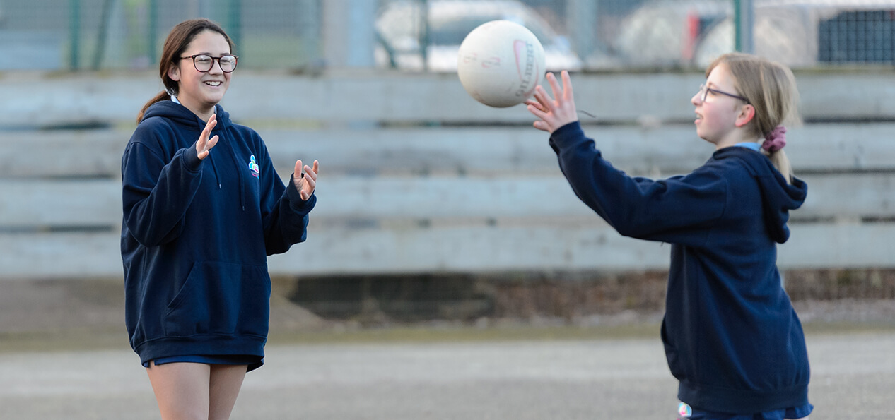 A schoolgirl throws a ball towards another girl during an outdoor game of netball.