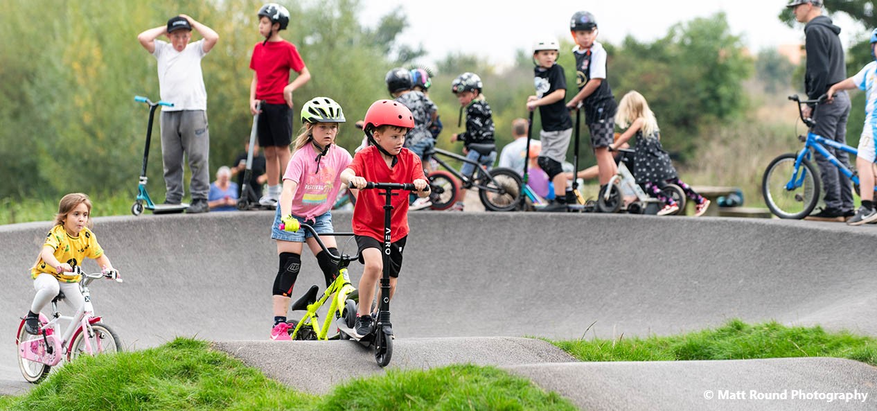 A group of kids play on a scooters park in Exeter during the Cranbrook Pump Track launch event in September 2024. Image credited to Matt Round Photography.