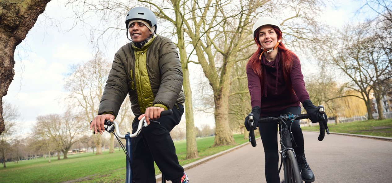 Two cyclists ride side by side in a park