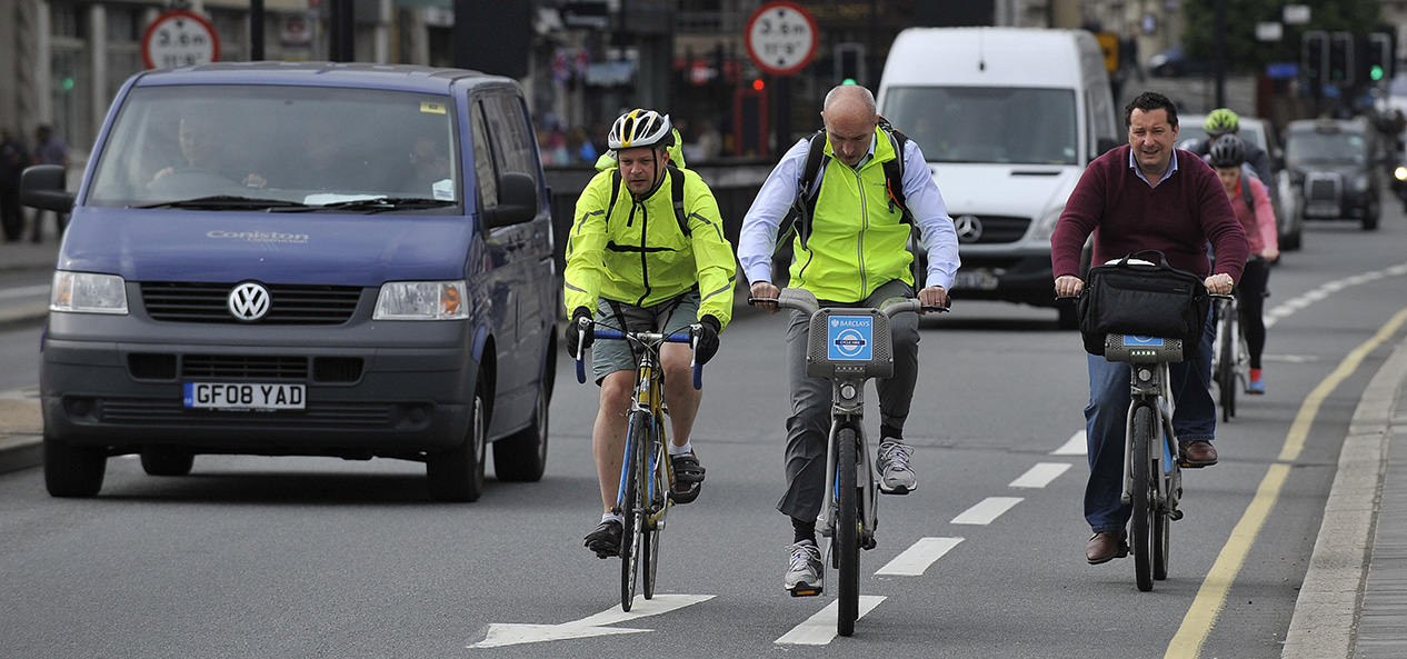 Cyclists, some on public hire bikes, share the road with cars in a city centre