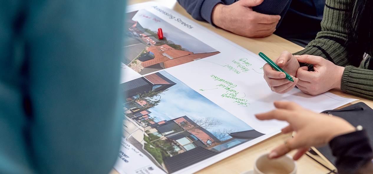 An overhead photo of a table during a planning workshop, on which are people's hands and an annotated diagram of a development