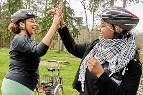 Two women high-five each other next to their bikes on a forest.