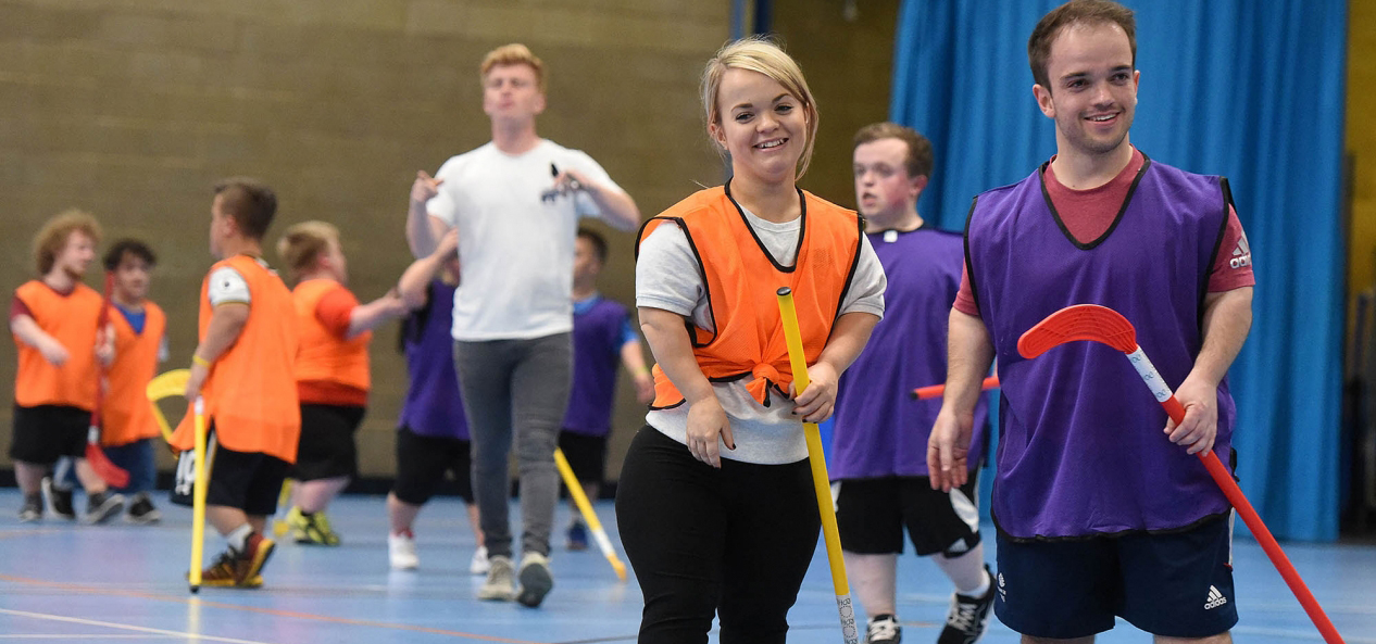 Two people in a sports hall playing hockey.