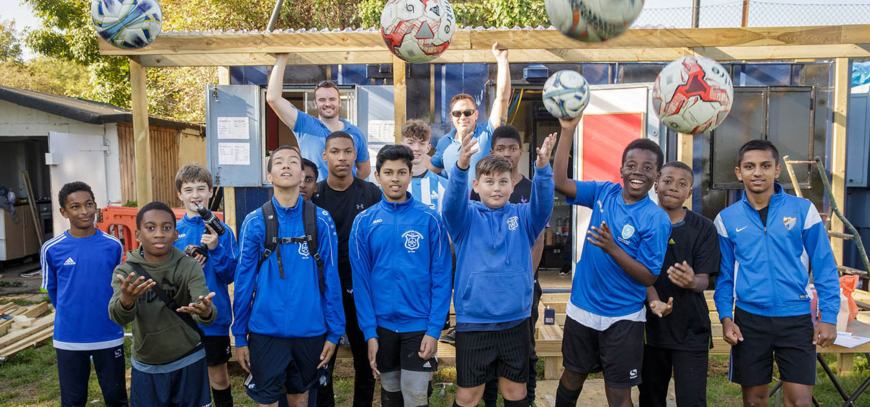 A group of boys at a Volunteer it Yourself project, building a clubhouse, throw footballs at the camera