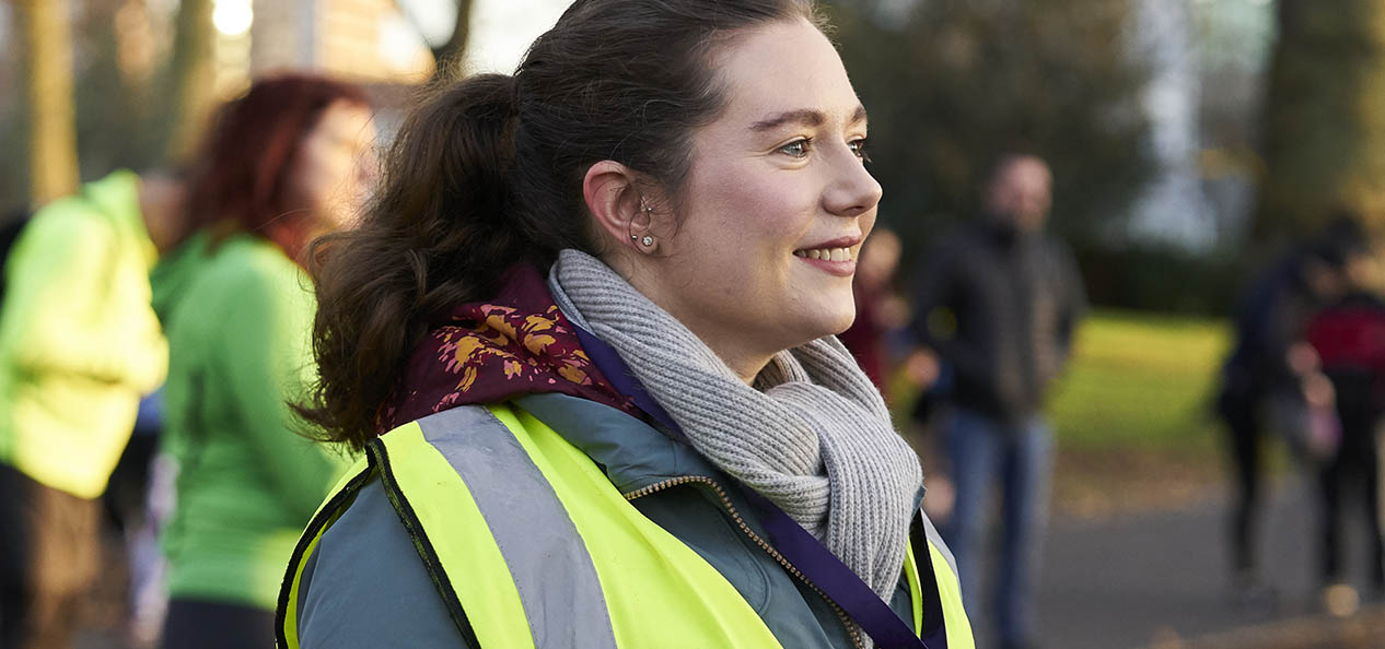 A female volunteer at a parkrun event, with a high-vis vest on and a whistle round her neck