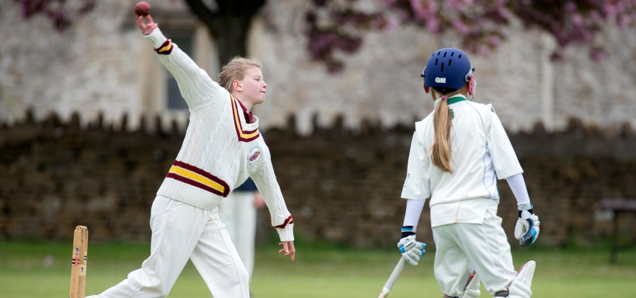 A girl bowls during a junior cricket match as a batter watches on