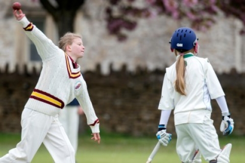 A girl bowls during a junior cricket match as a batter watches on