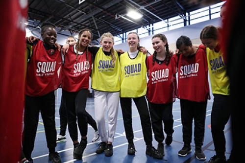 A group of teenage girls gather in a huddle at an indoor football session