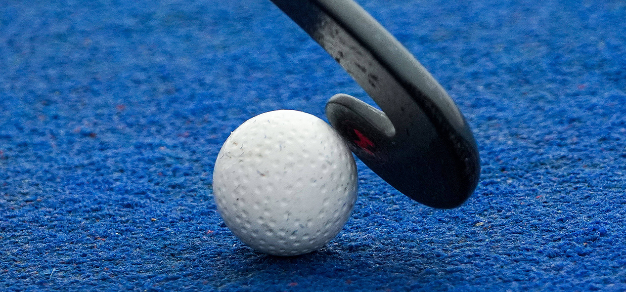 A close up of the head of a hockey stick on a hockey ball - on a blue hockey pitch