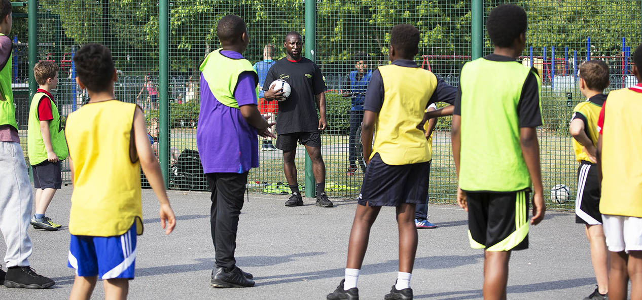 A group of boys listen to an instructor during a football session in a playground