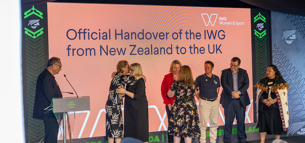 Delegates embrace on stage as the IWG on Women and Sport is handed over from Aotearoa New Zealand to the UK at an event at the Birmingham 2022 Commonwealth Games