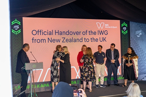 Delegates embrace on stage as the IWG on Women and Sport is handed over from Aotearoa New Zealand to the UK at an event at the Birmingham 2022 Commonwealth Games