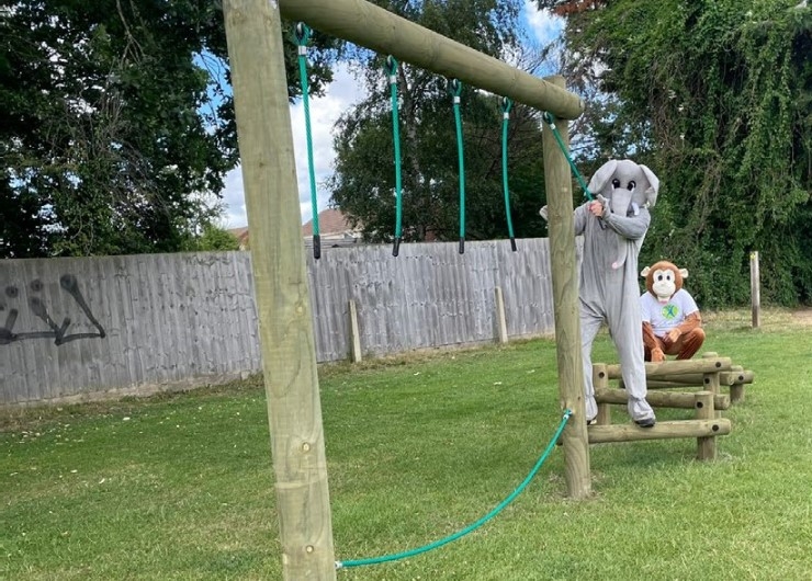 A person in an elephant suit on a park trim trail, alongside a person in a monkey suit.